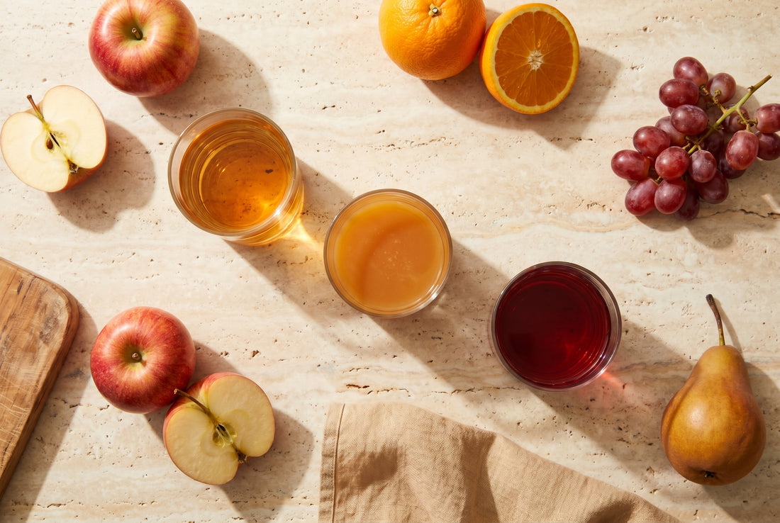 Drei Direktsäfte (Apfel, Orange, Trauben) mit frischen Früchten