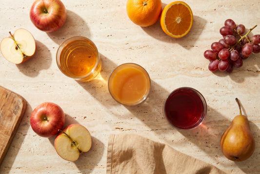 Drei Direktsäfte (Apfel, Orange, Trauben) mit frischen Früchten