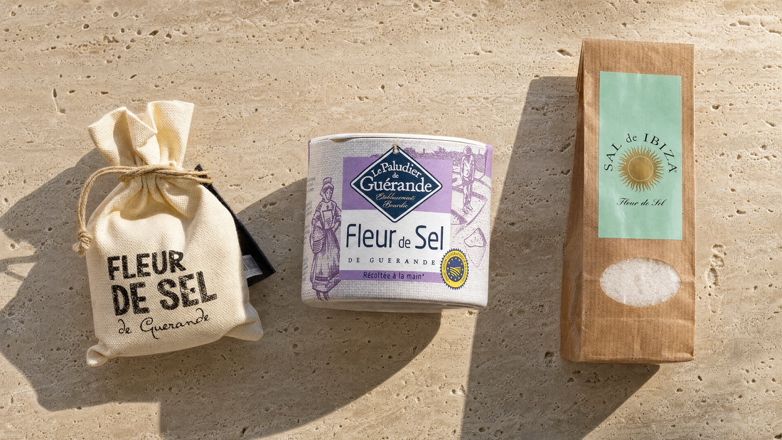 Fleur de Sel de Guérande im Leinensack, Le Paludier Fleur de Sel de Guérande und Sal de Ibiza Fleur de Sel im Nachfüllbeutel auf hellem Travertin