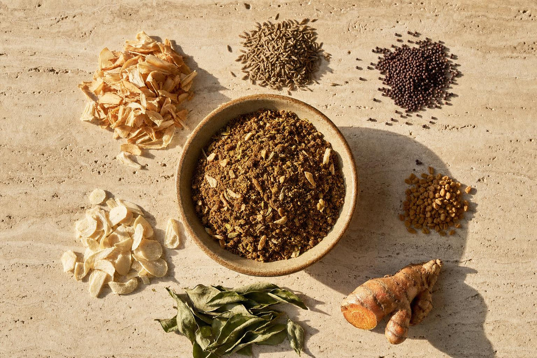 Vadouvan Gewürzmischung in einer Schale, daneben die Zutaten: getrocknete Zwiebeln, Knoblauch, Kreuzkümmel, Senfsaat, Bockshornklee, Curryblätter und Kurkuma