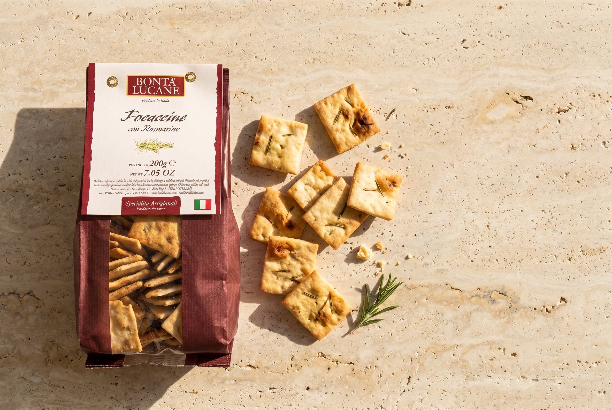 Bontà Lucane Focaccine al rosmarino auf Travertin-Tischplatte — lose Focaccine und Produkttüte